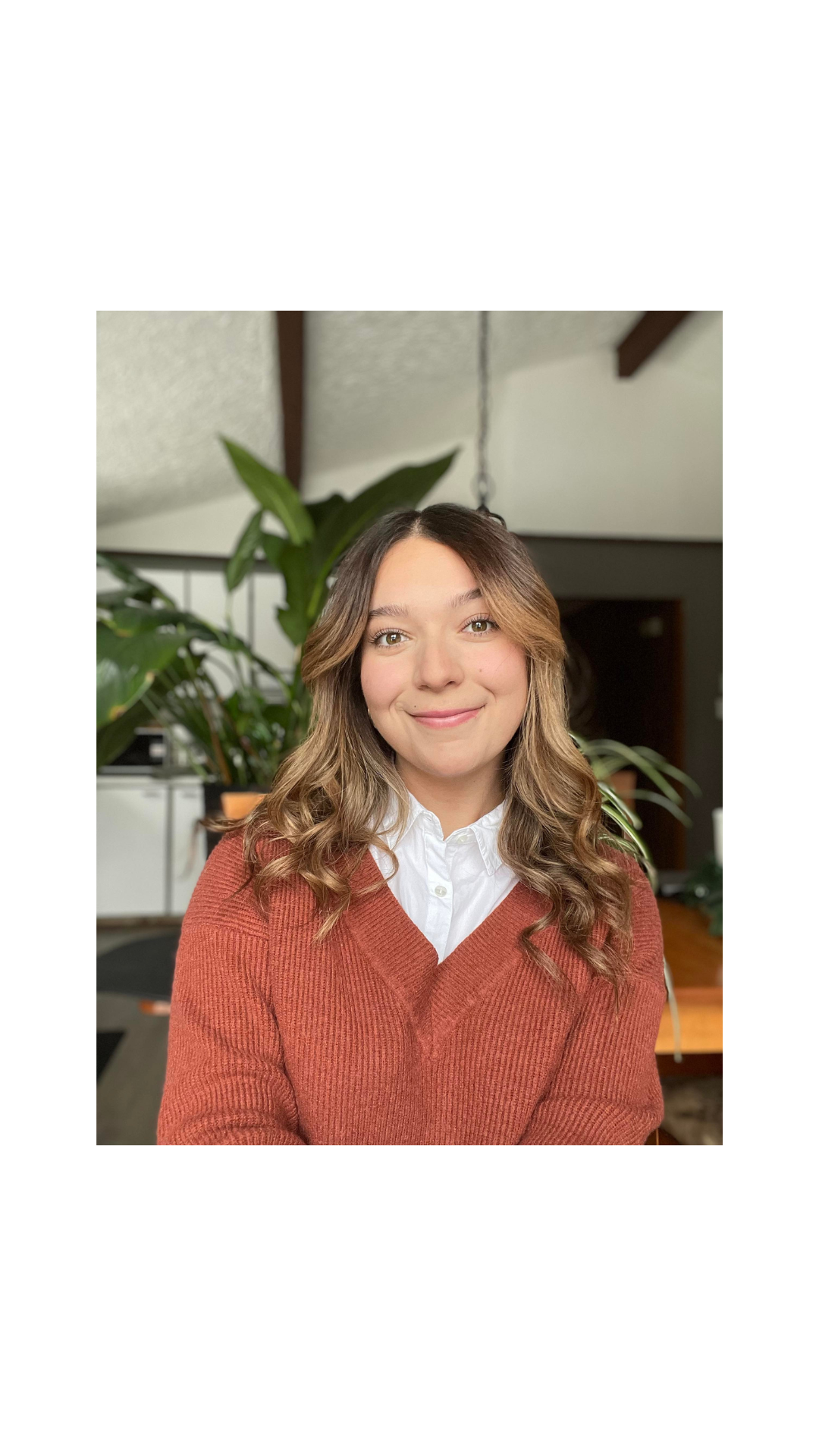 Portrait d’Audrey Paiement qui sourit et qui porte un cardigan orange brûlé devant des plantes.
