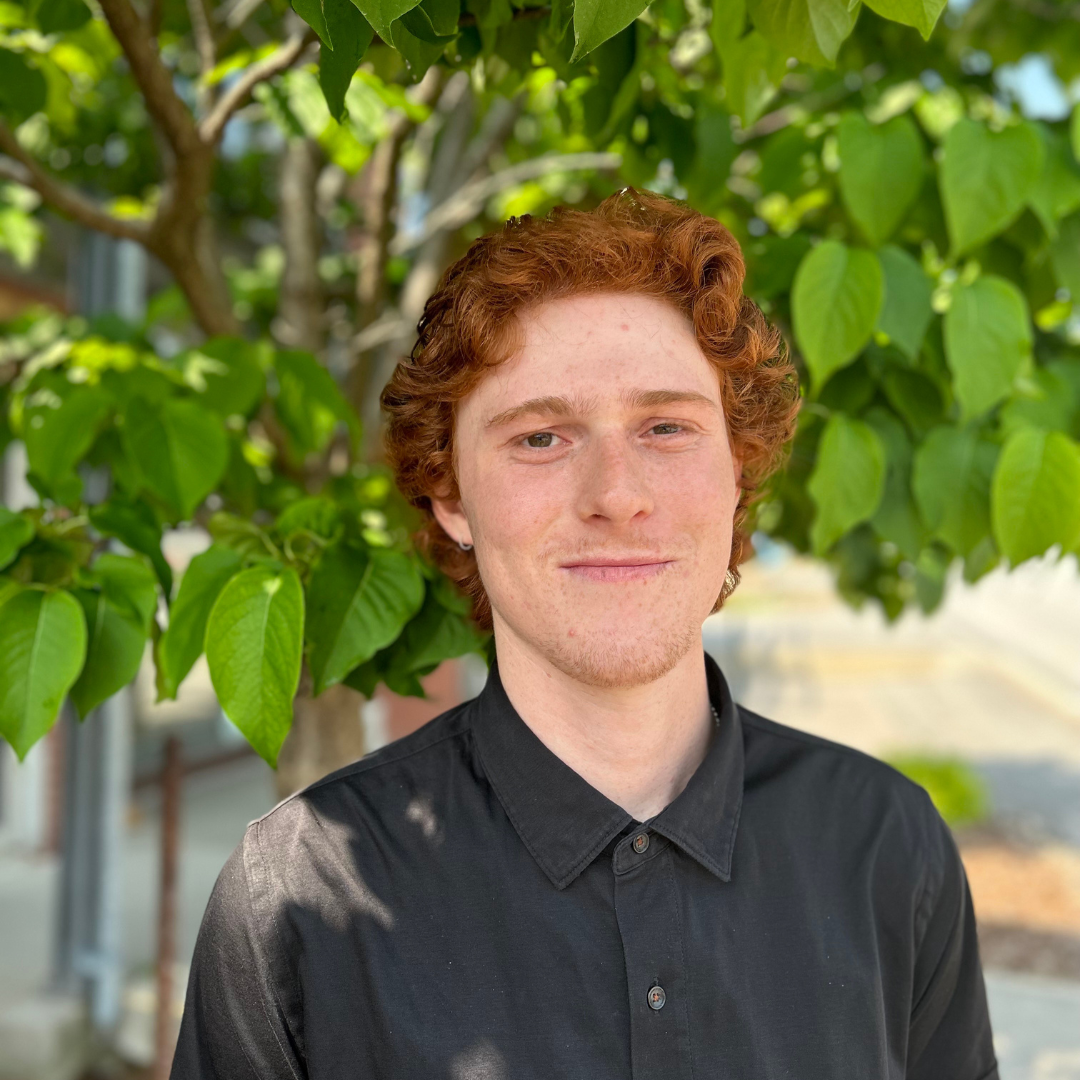 Portrait de Xavier St-Pierre qui porte une chemise noire et sourit devant un arbre.